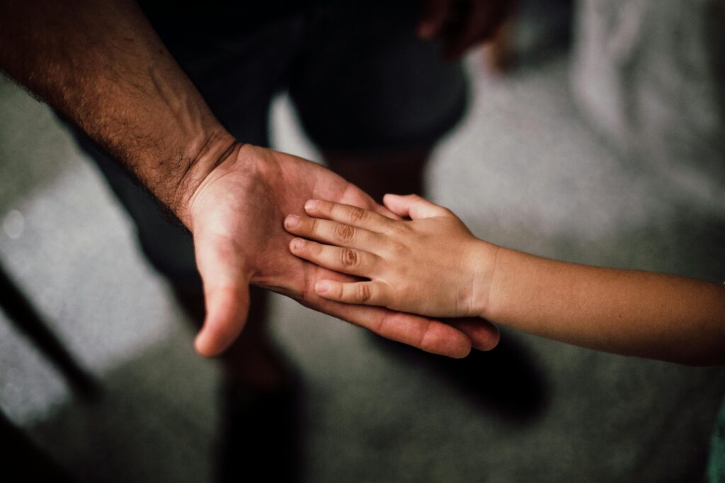 pexels-photo-1250452-1250452 Close-up of a child's hand resting gently on a man's hand, symbolizing love and support.